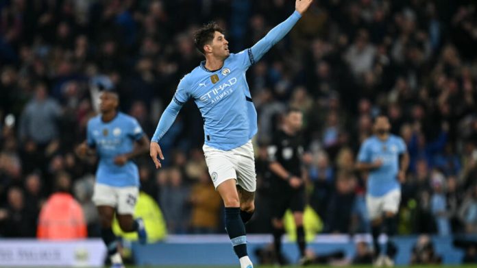 John Stones celebrating after scoring a late equaliser for Manchester City against Arsenal, arms raised in jubilation.