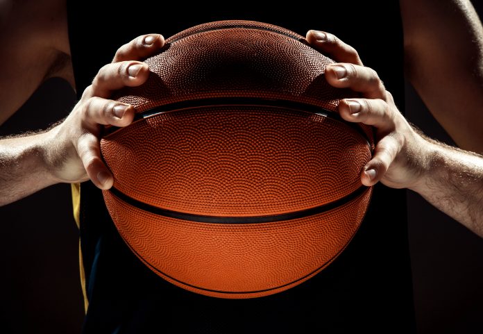 A striking silhouette of a basketball being held in one hand, symbolizing focus and control in the game.