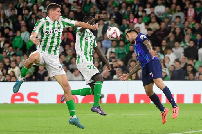 Atletico Madrid's Argentine forward #10 Angel Correa (R) heads the ball past Real Betis' Senegalese defender #23 Youssouf Sabaly (C) during the Spanish league football match between Real Betis and Club Atletico de Madrid at the Benito Villamarin stadium in Seville on October 27, 2024. (Photo by CRISTINA QUICLER / AFP)