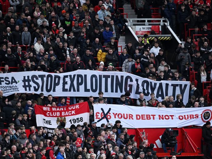 Fans of Manchester United display banners in protest of rising ticket prices as both teams make their way onto the pitch prior to the Emirates FA Cup Fifth Round match between Manchester United and Fulham at Old Trafford